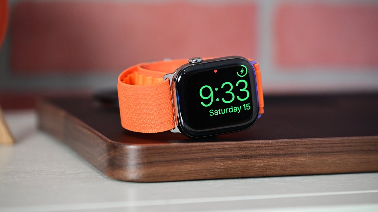 Smartwatch with an orange band displays time as 9:33 and date as Saturday 15 on a wooden surface.