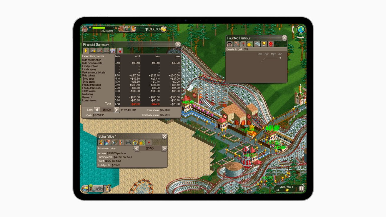Tablet displaying a theme park simulation game with financial summary and various park structures, including roller coasters and colorful attractions, surrounded by trees.